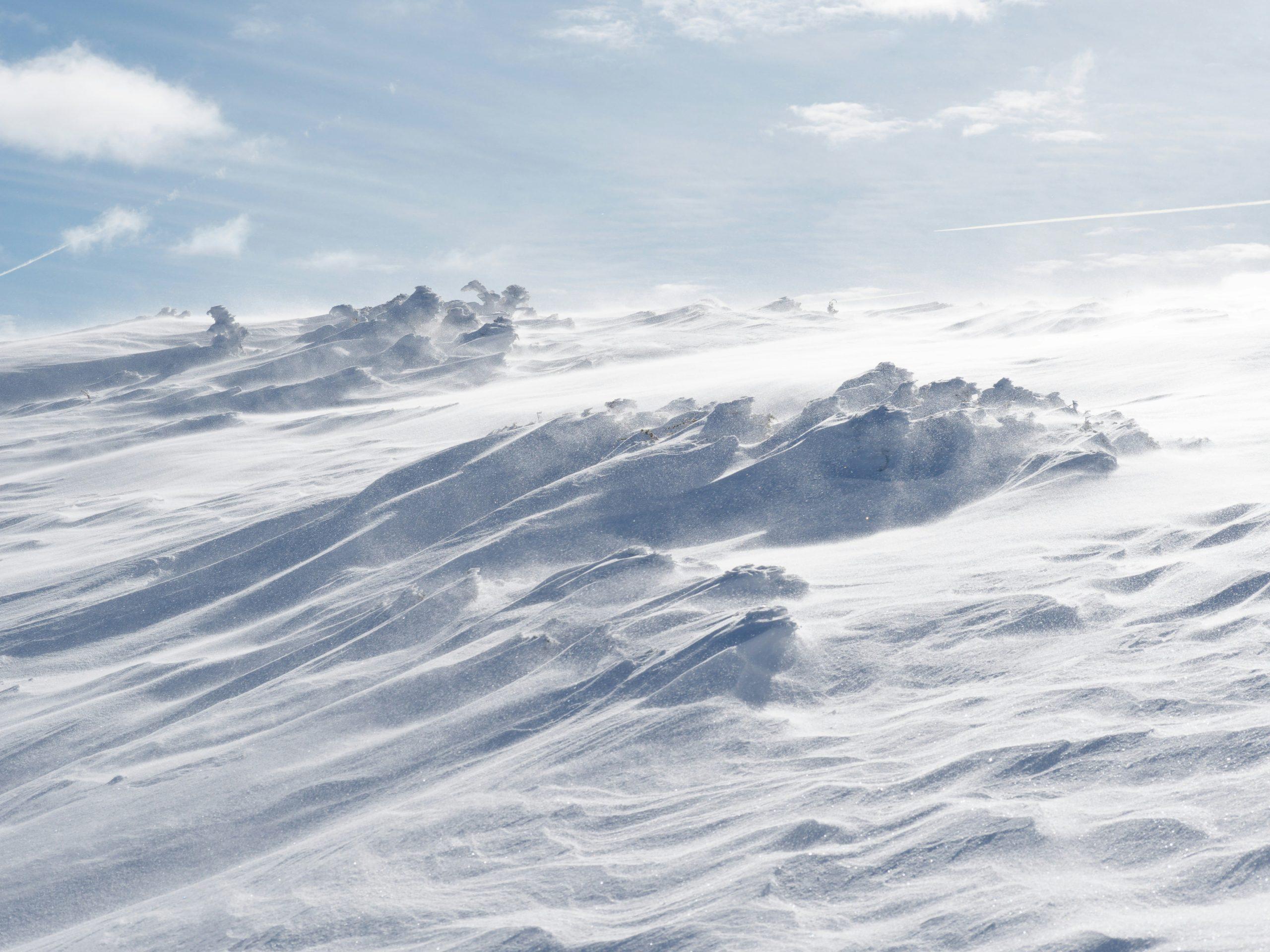 Wind-swept snow drifts on a frozen plateau under a blue sky with light clouds